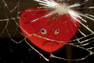 Red heart with a sad face reflected in a broken mirror with a black background