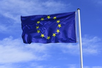 The flag of the EU European Union flutters in the wind against a blue cloudless sky