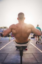 A man exercises outdoors in the sunlight, concentrating on strengthening his back muscles on a