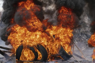 Burning automobile tires, strong flame of red fire and clouds of black smoke in sky. Selective