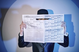 Man hiding watches through the newspaper in the spotlight on studio background. noir film style.