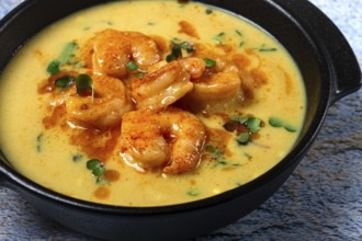 Creamy shrimp curry with spices, garnished with herbs, on a textured background, homemade, no