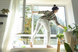 Woman manually washes the window of the house with a rag with spray cleaner and mop inside the