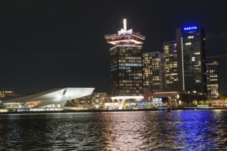 Illuminated skyline at night along a body of water with modern architecture and lights, Amsterdam,
