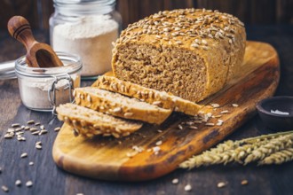 Homemade wholemeal spelt bread with sunflower seeds and baking ingredients on wooden background