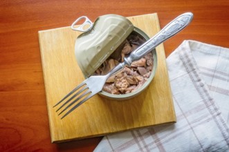 An open tuna box on a wooden board, with a fork and a towel