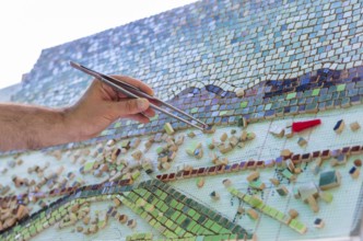 Mosaic as a ceramic or ceramic mosaic. The man organizes design with a tweezers a puzzle of ceramic