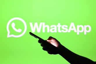 In this photo illustration the WhatsApp logo seen in the background of a silhouette hand holding a