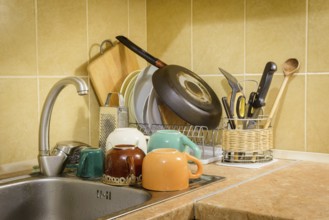 Dishes, cups, glasses, plates, forks, knives and spoons are drying close to the sink, after they