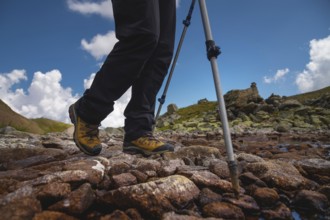 Hiking boots close-up on mountain rocks by the lake with trekking poles, view from below