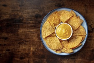 Nachos, Mexican tortilla chips, shot from above on a wooden background with a cheese dip