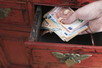hand taking stack of paper money from drawer of antique cabinet
