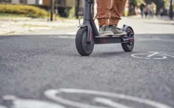 Young man in casual trousers riding an electric scooter detail on his feet and wheel over asphalt