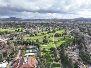 Aerial view of residential neighborhood surrounded by golf and valley during cloudy day in Rancho