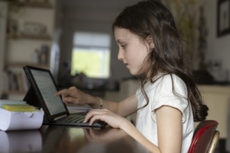 Girl, 10 years old, sits at the table with a tablet and learns