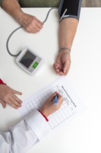 Doctor taking notes on blood pressure log book while measuring blood pressure of senior woman