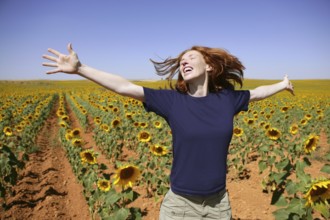 Happy redhead woman in sunflowers field outdoors