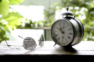 Old alarm bell clock at the window backlit in a house room with plants