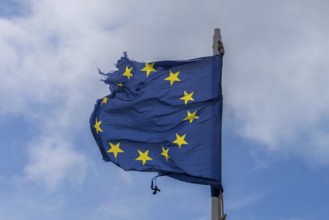 A torn EU flag blows in the wind with a few clouds in the background, seen in Pevensey Bay, East