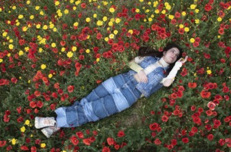 Young happy girl resting in the field of red poppy flowers. Drone aerial of woman in spring
