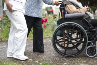 Senior woman in wheel chair with relative and nurse caregiver, outdoors at nursing home garden.