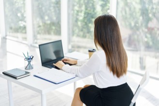 Back view of young businesswoman working with laptop in modern office