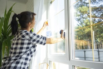 Woman manually washes the window of the house with a rag with spray cleaner and mop inside the