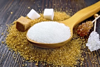 Sugar white and brown in cubes, crystal on a stick and granulated in a spoon on a wooden plank