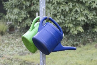 Blue and green watering cans hanging on a metal stand outdoors