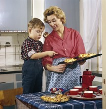Baking in the 1950s. A mother with her son in the kitchen. She has freshly baked buns and cakes