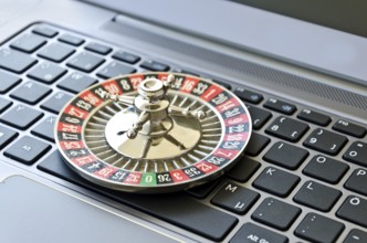 Roulette wheel lying on computer keyboard symbolizing online gambling