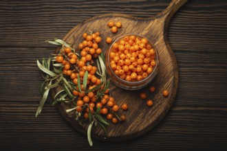 Sea buckthorn ripe berries in glass jar and branches with leaves top view on dark wooden rustic
