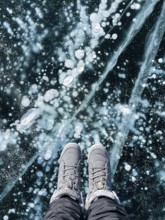 Fragile thin brittle ice underfoot. Female feet on ice. Woman wearing winter shoes on ice of