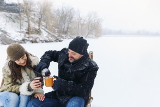Happy lovely middle-aged couple in warm clothes drinking hot tea during romantic winter date in
