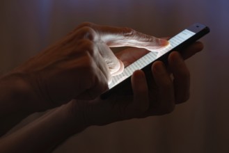 Man typing with the finger on the touch screen of a black smartphone close to the window with