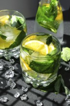 Mojito refreshing cocktail, alcohol drink. Lemonade with lemon and mint leaves on dark background.