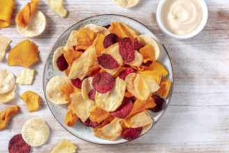 Various vegetable chips with a homemade dip, shot from the top on a rustic wooden background with a