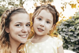 Cute little redhead girl and happy young mother with similar braided hairdo hugging together