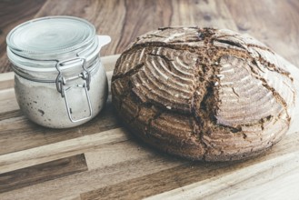 Freshly baked homemade rye sourdough bread and sourdough starter in jar on wooden table