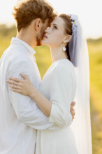 A couple sharing an affectionate moment outdoors in wedding attire, warm lighting