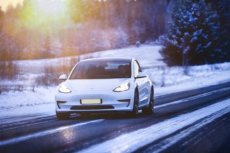 White Tesla Model 3 electric car at speed on highway in winter at dusk. Salo, Finland. December 27,