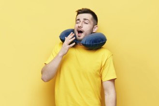 Tired young man yawning with travel pillow on yellow background. tourism, rest concept