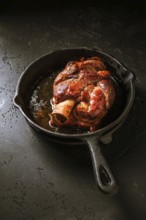 Traditional German cuisine - Roasted pork knuckle eisbein (Schweinshaxe) in iron pan on black