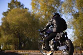 Male motorcyclist in a leather jacket and helmet on a vintage custom motorcycle in nature. Concept