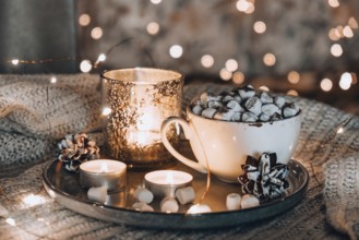 Cup with hot winter cacao and marshmallows on bed. Christmas lights. Pine cones decoration. Cozy