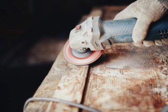 Close-up of an angle grinder being used on a wooden table by a gloved hand