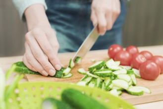 Close-up of female hands cut into fresh cut cucumbers on a wooden cutting board next to pink