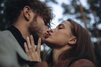 A close-up of a romantic kiss between a couple in a forest environment