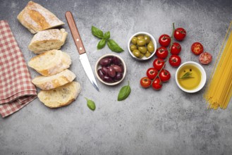 Food composition with sliced ciabatta, olives, olive oil, spaghetti, fresh basil, cherry tomatoes