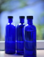 Three Blue glass body oil bottles in bathroom window